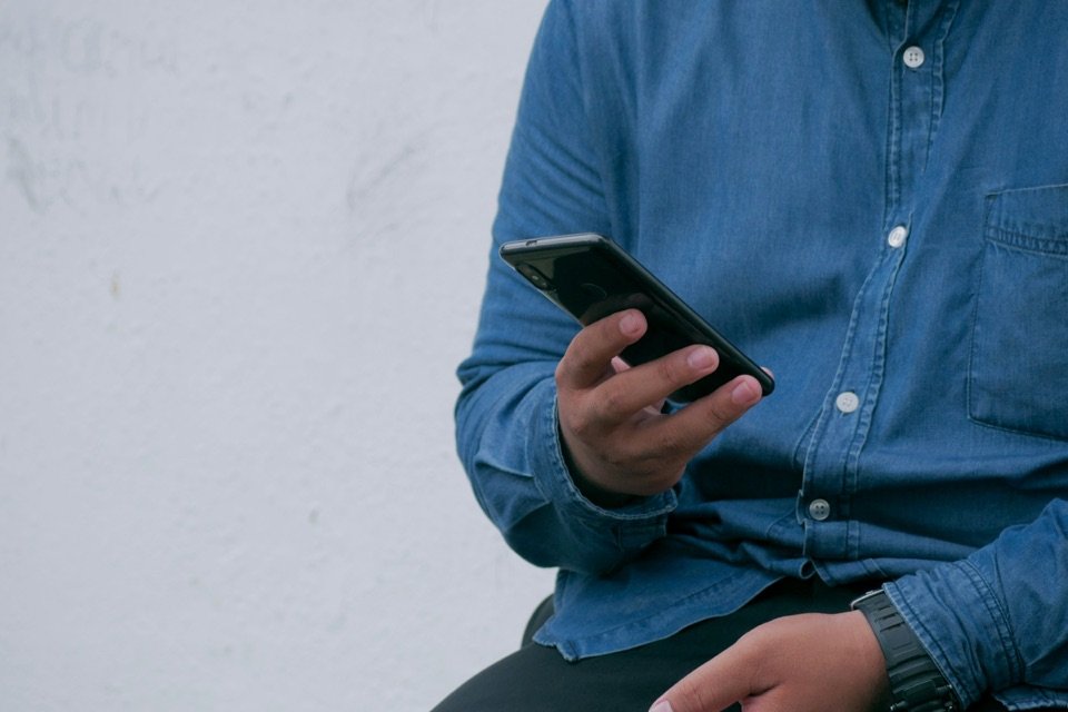 Un homme en chemise en jean consulte son téléphone.