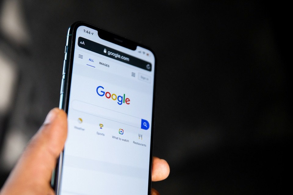 Une main tient un smartphone ouvert sur la page d'accueil de Google.